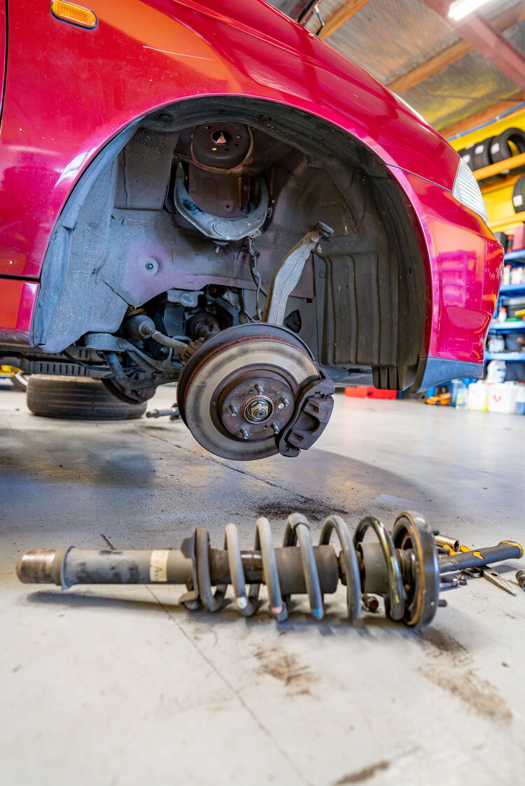 Front suspension removed from a red car at Hamilton Auto Centre workshop