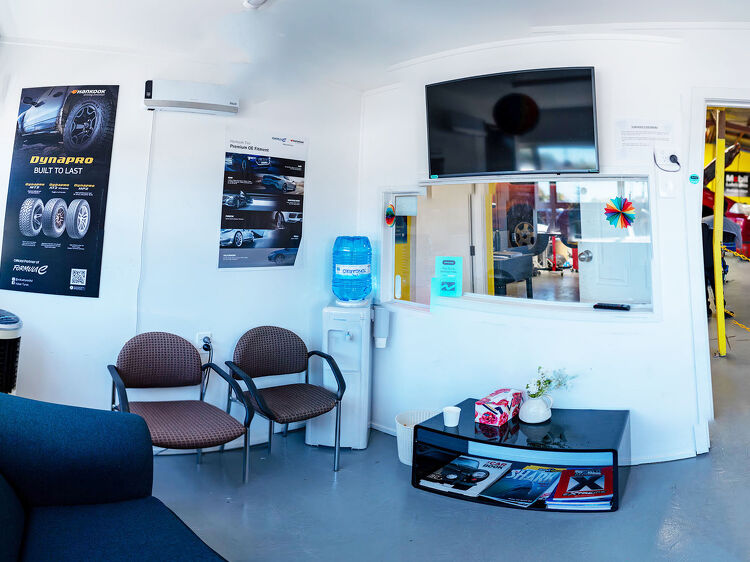 Reception and waiting area at Hamilton Auto Centre with chairs, TV, and water dispenser overlooking the workshop